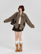 Person wearing a brown textured coat, black skirt, and brown boots on a gray background